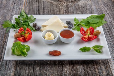 Geleneksel Türk kahvaltı tabağı gri ahşap masada, üst görünüm: sebzeler, peynirler, zeytinler, bal, tereyağı, seçici odak; metin alanı için kopyalama.