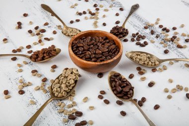 Beyaz ahşap masadaki kahve çekirdekleri için çeşitli kaliteli kaşıklar. Çiğ, hafif kavrulmuş ve çift kavrulmuş kahve çekirdekleri..