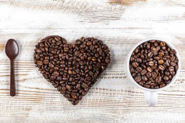 Bir fincan kahve, kahve çekirdeğinden yapılmış kalp şekli ve tahta arka planda çikolata kaşığı. Kahveye Aşkın Sembolü.