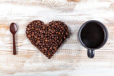 Bir fincan kahve, kahve çekirdeğinden yapılmış kalp şekli ve tahta arka planda çikolata kaşığı. Kahveye Aşkın Sembolü.