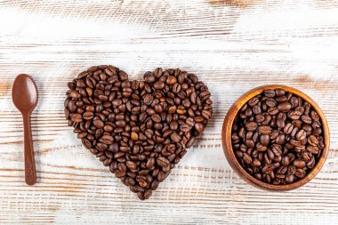 Bir fincan kahve, kahve çekirdeğinden yapılmış kalp şekli ve tahta arka planda çikolata kaşığı. Kahveye Aşkın Sembolü.