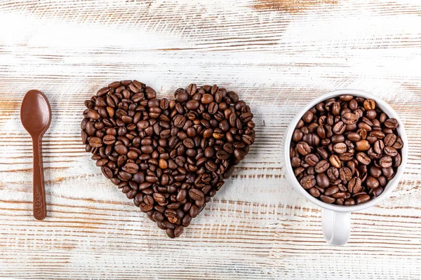 Cup of coffee, heart shape made from coffee beans and chocolate spoon on wooden background. Symbol of Love to coffee.