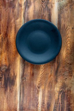 Ahşap masada siyah boş servis tabağı. Ahşap zemin üzerinde siyah yuvarlak tabak, üst görünüm, kopyalama alanı.
