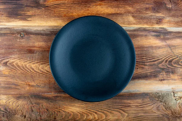 Black empty serving plate on the wooden table. Black round plate on wooden background, top view, copy space.