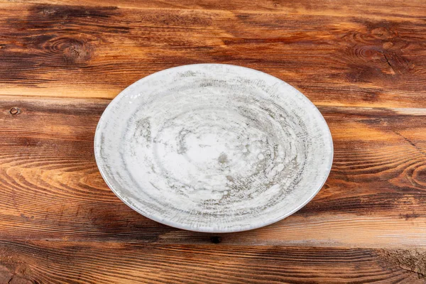 White serving plate on the wooden table. Empty plate on old wooden background. Top view