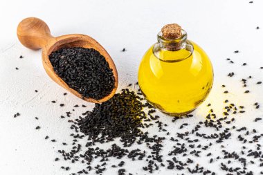 Tahta arka planda tohumları olan siyah kimyon yağı. Cam şişe siyah kimyon tohumları esaslı yağ, Nigella Sativa kaşıkta ve ahşap arka planda kase..