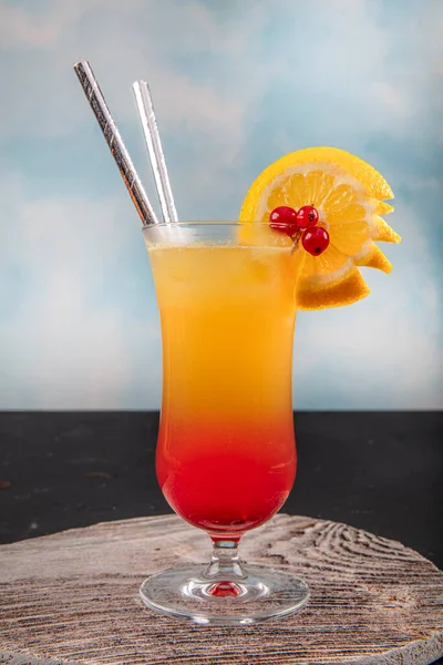 Juicy Orange and Red Tequila Sunrise with a Cherry. Tequila sunrise cocktail on dark wooden table.