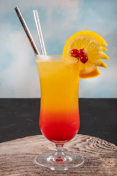 Juicy Orange and Red Tequila Sunrise with a Cherry. Tequila sunrise cocktail on dark wooden table.