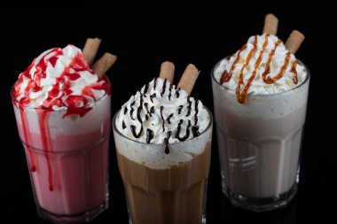 Üç bardak renkli milkshake kokteyli - çikolata, çilek ve vanilya, siyah arka planda izole edilmiş..