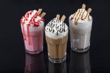 Üç bardak renkli milkshake kokteyli - çikolata, çilek ve vanilya, siyah arka planda izole edilmiş..