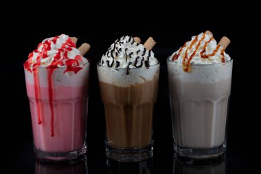 Üç bardak renkli milkshake kokteyli - çikolata, çilek ve vanilya, siyah arka planda izole edilmiş..