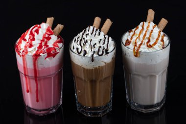 Üç bardak renkli milkshake kokteyli - çikolata, çilek ve vanilya, siyah arka planda izole edilmiş..