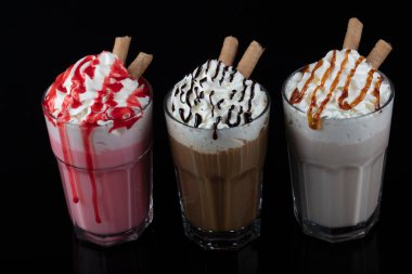 Üç bardak renkli milkshake kokteyli - çikolata, çilek ve vanilya, siyah arka planda izole edilmiş..
