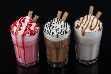Üç bardak renkli milkshake kokteyli - çikolata, çilek ve vanilya, siyah arka planda izole edilmiş..