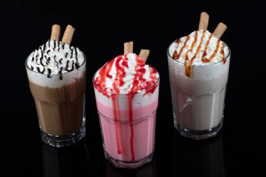 Üç bardak renkli milkshake kokteyli - çikolata, çilek ve vanilya, siyah arka planda izole edilmiş..