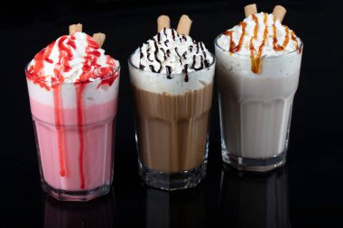 Üç bardak renkli milkshake kokteyli - çikolata, çilek ve vanilya, siyah arka planda izole edilmiş..