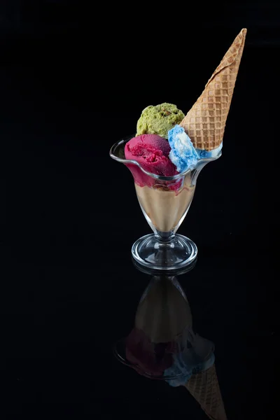 Fruit ice cream scoops overhead on a cornet, served with several colorful spoons isolated on black background.