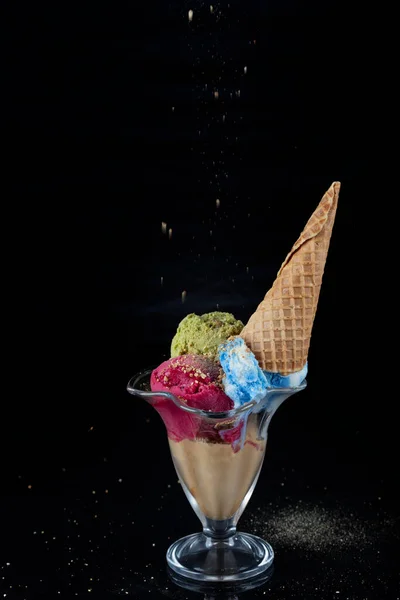 Fruit ice cream scoops overhead on a cornet, served with several colorful spoons isolated on black background.