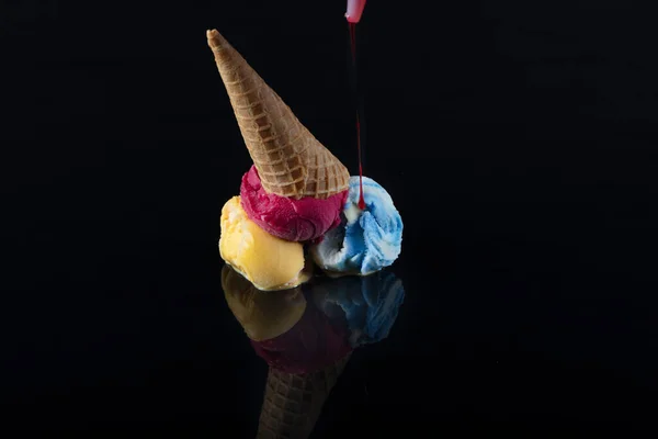 Fruit ice cream scoops overhead on a cornet, served with several colorful spoons isolated on black background.