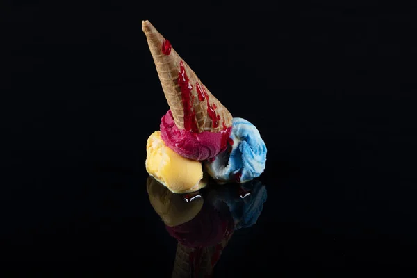 Fruit ice cream scoops overhead on a cornet, served with several colorful spoons isolated on black background.