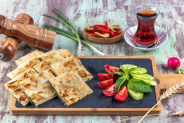 Taze pişmiş Türk tortillası - Tahta üzerinde ıspanaklı Gözleme ve Türk çayı. Mesaj için yer var. Yüzeyin derinliği. El yapımı Türk geleneksel pastaları.