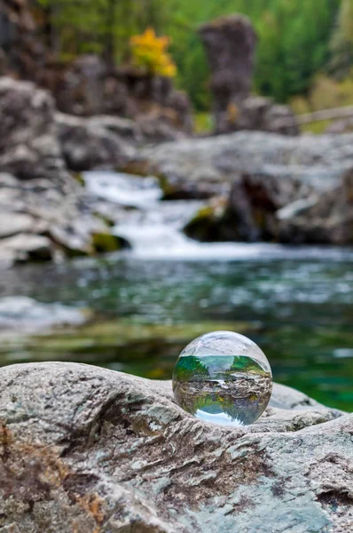 Crystal glass ball sphere sitting on rock with waterfall in background