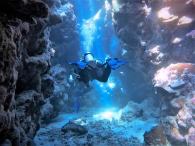 Mercan resifinin altındaki tüneldeki bir tüplü dalgıcın güzel güneş ışığıyla çekilmiş su altı fotoğrafı. Mısır 'daki Kızıl Deniz' deki bir dalıştan.. 