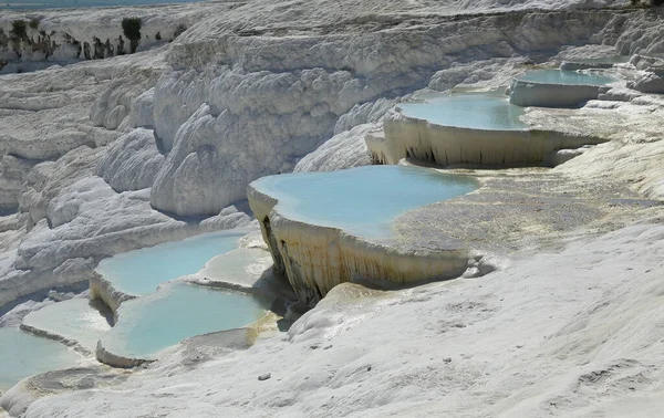 Pamukkale, Türkiye. Bu bölge, zengin karbonatlı su kaynaklarından gelen su nedeniyle kaya yapısında beyaz kalıntı bırakarak oluşan travertiniyle ünlü bir turistik şehirdir..