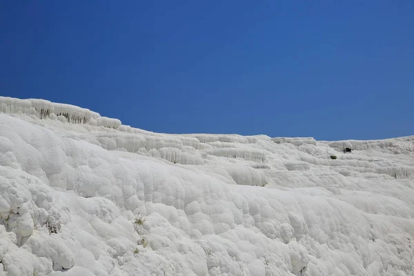 Pamukkale, Türkiye. Bu bölge, zengin karbonatlı su kaynaklarından gelen su nedeniyle kaya yapısında beyaz kalıntı bırakarak oluşan travertiniyle ünlü bir turistik şehirdir..