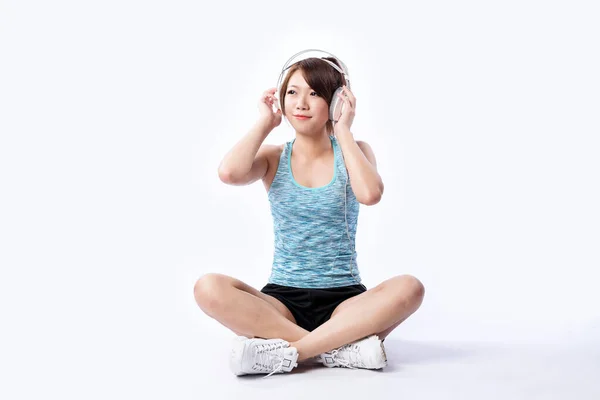 Young Asian girl sits on floor listening music with earphones.