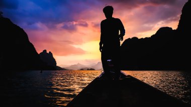 Tayland 'ın arka planında dramatik günbatımı bulutları olan teknede duran balıkçı silueti görüntüsü. 