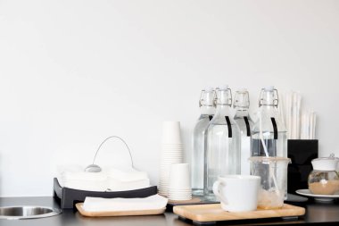 Temiz su şişelerini, seramik çimenleri ve peçeteyi evdeki beyaz duvar arkaplanlı ahşap masaya kurun..