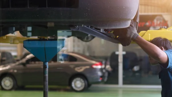 Professional car mechanic working under car to changing motor oil maintenance repair service station in a car workshop.