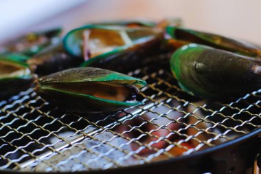 Kömür ızgarasında taze midyeleri kapayın, Tayland usulü baharatlı deniz ürünleri sosuyla daldırın.. 