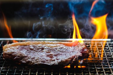 Çiğ et bifteği bbq ızgara kömür ocağında duman ve siyah arka planda ateş..