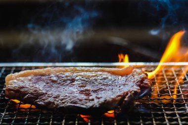 Çiğ et bifteği bbq ızgara kömür ocağında duman ve siyah arka planda ateş..