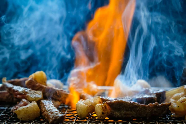 Çiğ et dilimlenmiş bbq ızgara kömür ocağı üzerinde duman ve siyah arka planda ateş.