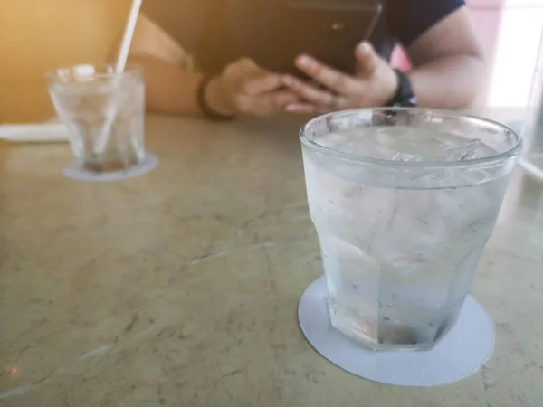 Sklenice Vody Studeným Ledem Stole Rozmazané Mladé Ženy Pomocí Smartphone — Stock fotografie