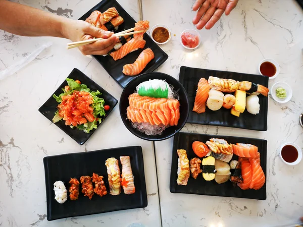 日本の伝統料理のトップビューレストランのテーブルの上に並べられた寿司ロール 竹棒を使って寿司ロールを食べる人の手 — ストック写真