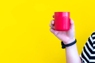 Sarı arka planda kırmızı bardağı tutan kadının eli. yiyecek ve içecek konsepti. Kopya alanı.