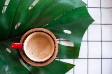  Üst manzara yeşil yapraklı kırmızı kahve fincanı ve beyaz şebeke kumaş arka planında siyah kupa..