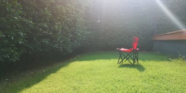 Kırmızı kamp koltuğu doğada taze yeşil çimen tarlasında, parlak güneş ışığı altında. , 