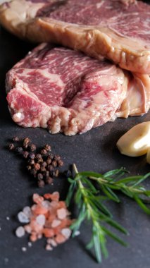 Taze et, biftek, domuz eti, siyah levha taşından yapılmış arka planda tuz, biber, biber, barbekü ve terbiye edilmiş et. Sağlıklı, doğal yiyecekler..