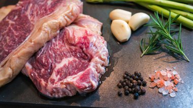 Taze et, biftek, domuz eti, siyah kayrak taşı kaplama arka planda tuzlu, biberli, sarımsaklı, kuşkonmaz ve barbekü soslu et. Sağlıklı yemek.