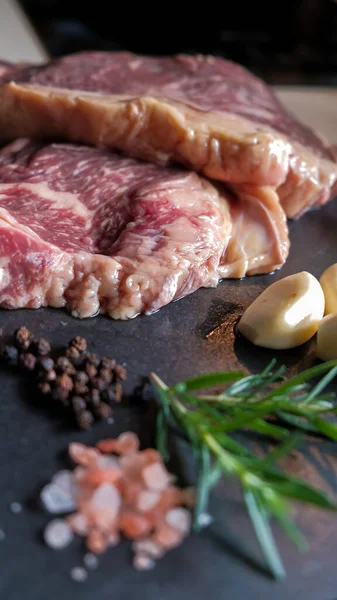 Taze et, biftek, domuz eti, siyah levha taşından yapılmış arka planda tuz, biber, biber, barbekü ve terbiye edilmiş et. Sağlıklı, doğal yiyecekler..