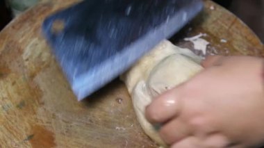 Şef eller büyük bıçaklar kullanarak tahtanın üzerinde haşlanmış tavuk etini kesmeye hazırlanıyor.