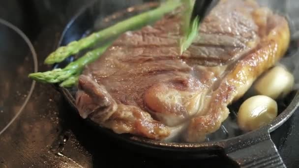 料理肉ステーキの新鮮なジューシーなスライスをつかむ材料スパイスを鍋に豚肉の牛肉塩コショウニンニクローズマリーアスパラと煙 — ストック動画