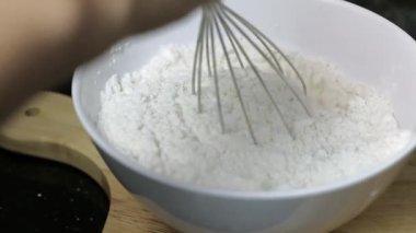El, mutfakta beyaz bir kaseye beyaz un döküyor, undan elde yapılan hamur işlemini tamamlıyor., 