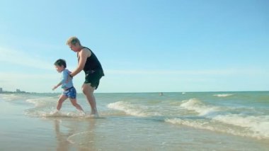 Mutlu aile babası ve oğlu kumlu tropikal sahilde birlikte yürüyorlar deniz mavisi gökyüzü arka planına karşı yazın Tayland 'da