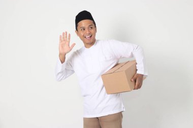 Koko gömlekli heyecanlı Asyalı Müslüman adamın portresi karton kutu taşırken selam veriyor, birine selam veriyor. Bayram için eve gidiyorum. Beyaz arkaplanda izole edilmiş resim